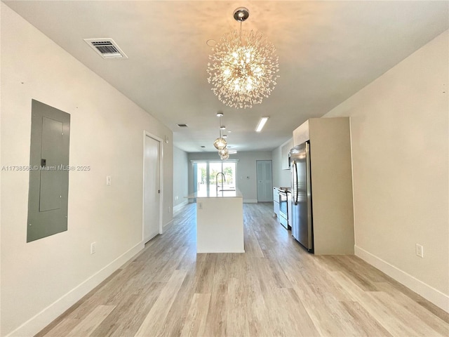 kitchen featuring an inviting chandelier, decorative light fixtures, light hardwood / wood-style flooring, appliances with stainless steel finishes, and electric panel