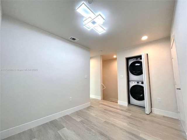 laundry area with stacked washer / drying machine and light hardwood / wood-style floors