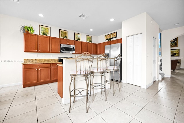 kitchen with light tile patterned floors, stainless steel appliances, a kitchen breakfast bar, and a center island