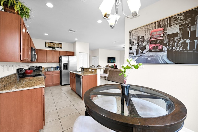 kitchen with appliances with stainless steel finishes, a kitchen island with sink, hanging light fixtures, light stone countertops, and light tile patterned flooring