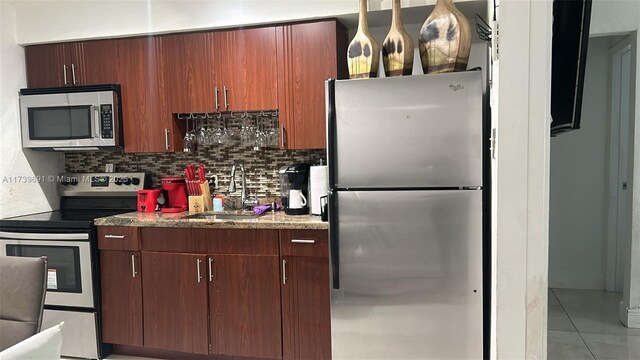 kitchen featuring sink, light tile patterned floors, stone counters, appliances with stainless steel finishes, and backsplash