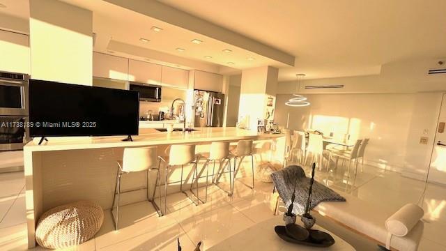 kitchen with stainless steel appliances, a sink, white cabinetry, a kitchen breakfast bar, and decorative light fixtures