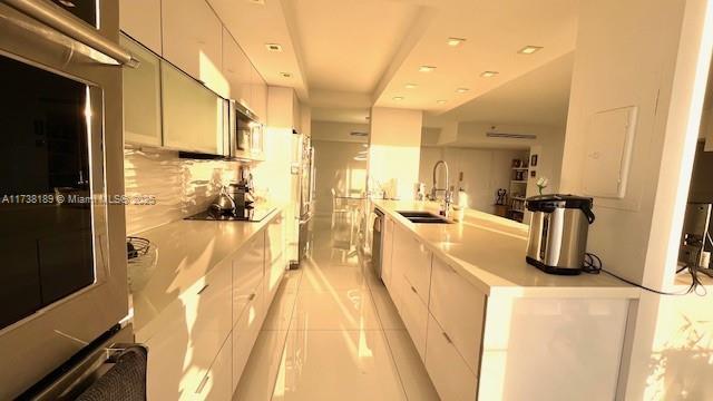 kitchen featuring a sink, stainless steel microwave, modern cabinets, and white cabinets