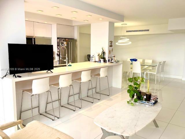 kitchen with a kitchen breakfast bar, white cabinets, high quality fridge, a peninsula, and light tile patterned floors