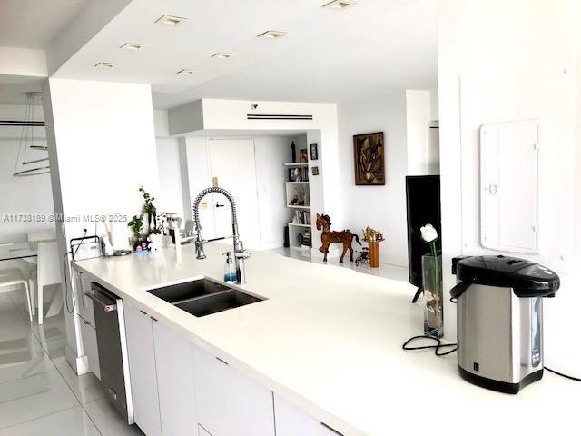 kitchen with a sink, stainless steel dishwasher, white cabinets, light countertops, and a peninsula