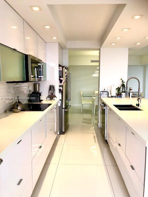 kitchen with appliances with stainless steel finishes, modern cabinets, a sink, white cabinetry, and light countertops