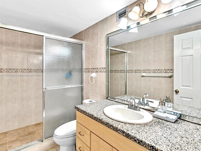 bathroom featuring a shower with door, vanity, tile walls, and toilet