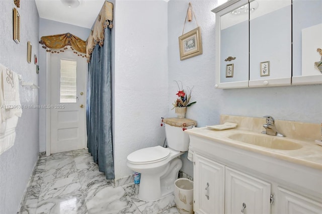 bathroom featuring marble finish floor, toilet, a textured wall, and vanity