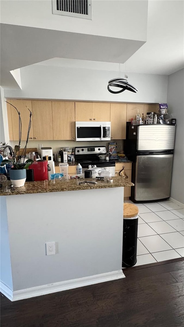 kitchen featuring dark stone countertops, stainless steel appliances, kitchen peninsula, and light brown cabinets