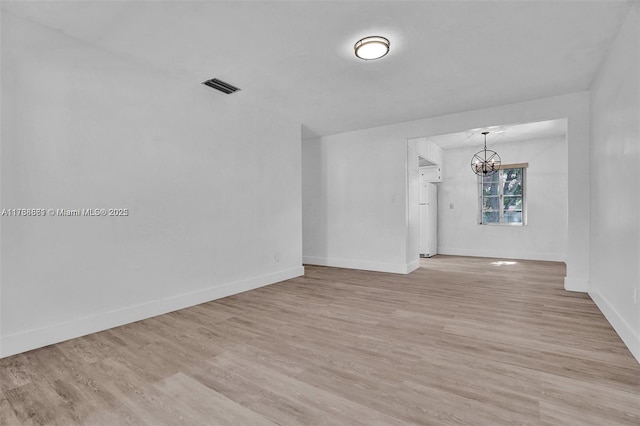 unfurnished room with a notable chandelier and light hardwood / wood-style floors