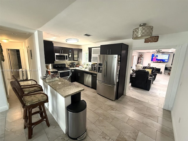 kitchen featuring a breakfast bar area, appliances with stainless steel finishes, light stone counters, tasteful backsplash, and kitchen peninsula