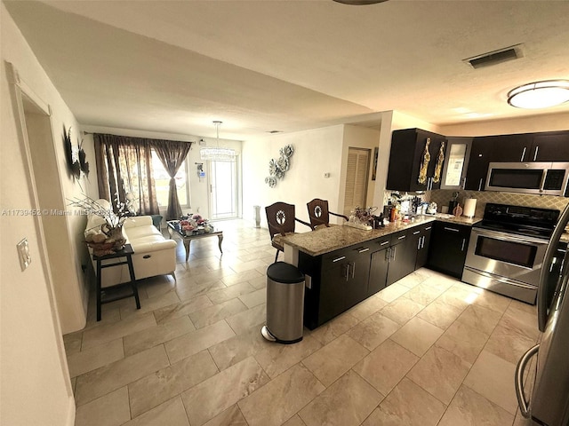 kitchen featuring appliances with stainless steel finishes, decorative light fixtures, decorative backsplash, kitchen peninsula, and light stone countertops