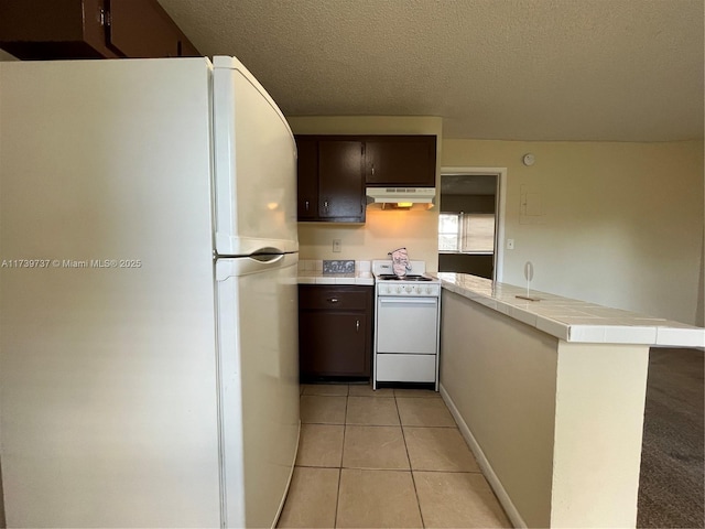 kitchen with white appliances, dark brown cabinetry, kitchen peninsula, and light tile patterned floors