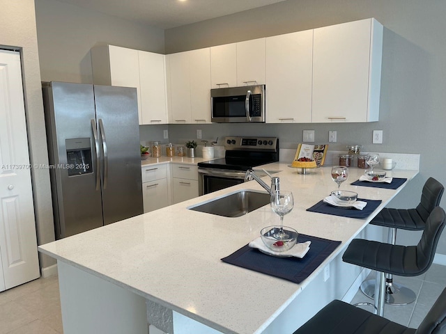 kitchen with a kitchen bar, sink, white cabinetry, appliances with stainless steel finishes, and kitchen peninsula