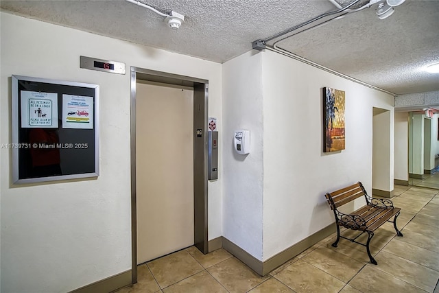 hallway with elevator, a textured ceiling, and light tile patterned floors