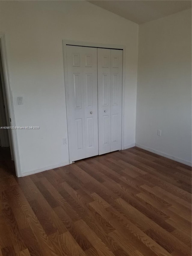 unfurnished bedroom with lofted ceiling, dark wood-type flooring, and a closet