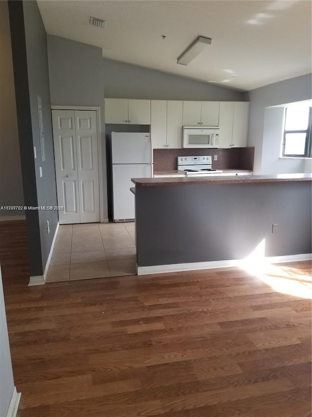 kitchen with lofted ceiling, white appliances, white cabinetry, hardwood / wood-style floors, and tasteful backsplash