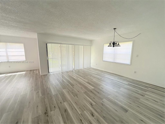 empty room featuring light wood-type flooring, an inviting chandelier, and a textured ceiling