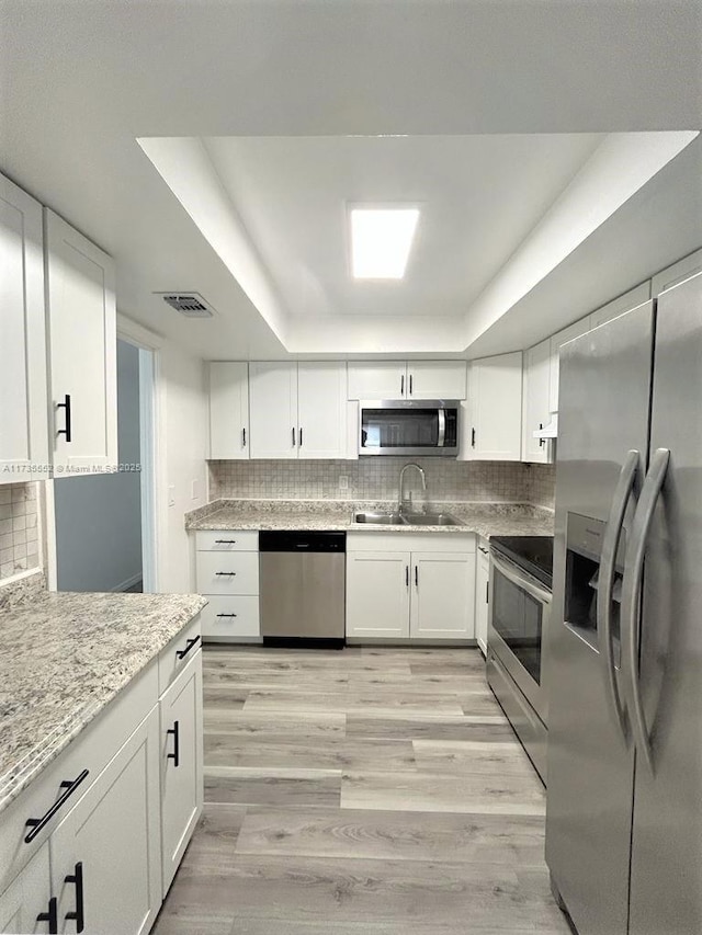 kitchen featuring a raised ceiling, sink, stainless steel appliances, and white cabinetry