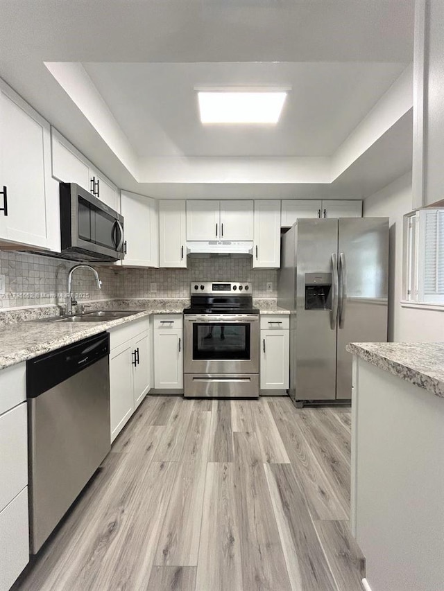 kitchen with a raised ceiling, appliances with stainless steel finishes, white cabinetry, and tasteful backsplash