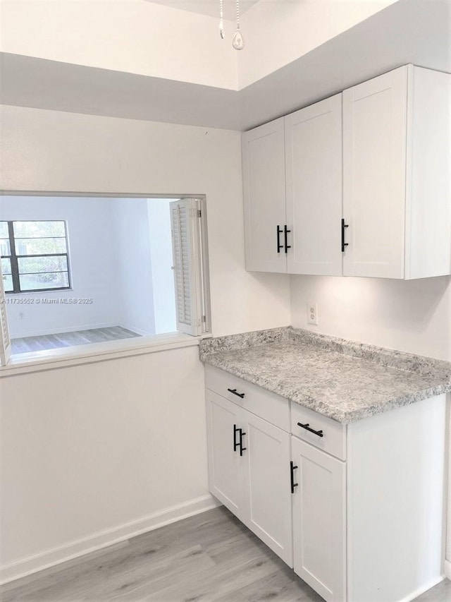 kitchen with white cabinets, light stone counters, and light hardwood / wood-style flooring