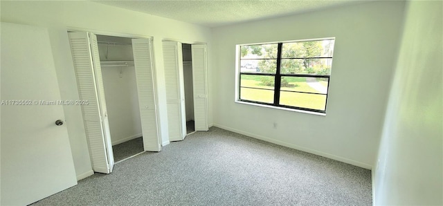 unfurnished bedroom with two closets, a textured ceiling, and light colored carpet