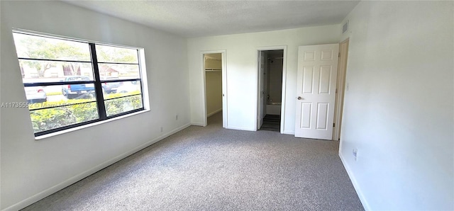 unfurnished bedroom featuring a closet, carpet, a walk in closet, and a textured ceiling