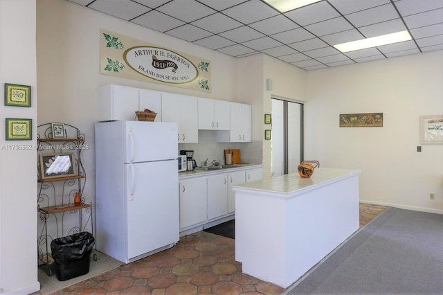 kitchen featuring white cabinetry, sink, white fridge, decorative backsplash, and a drop ceiling