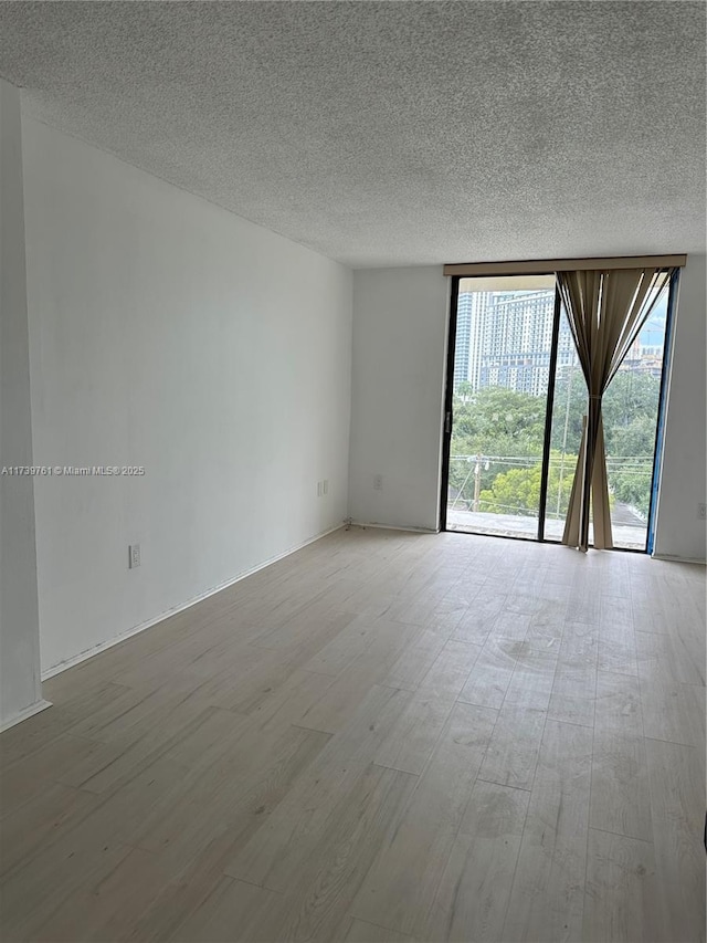 empty room featuring a wall of windows, a textured ceiling, and light wood-type flooring