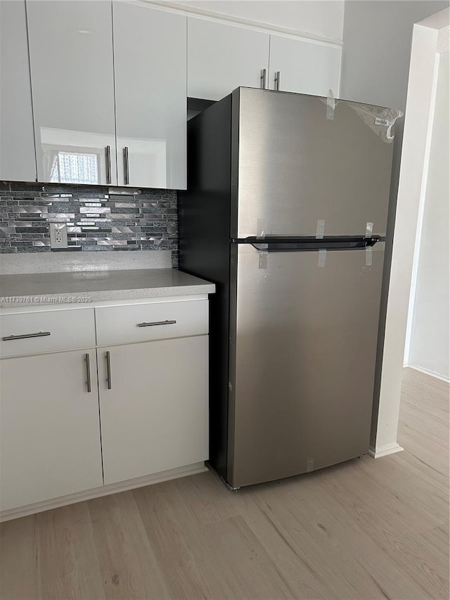 kitchen with white cabinetry, decorative backsplash, stainless steel fridge, and light hardwood / wood-style floors