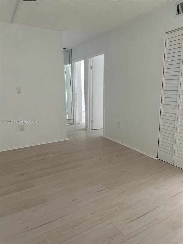 unfurnished room featuring a textured ceiling and light hardwood / wood-style flooring