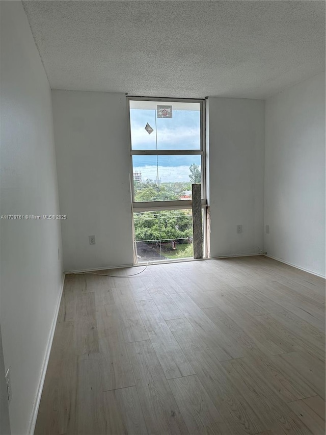 empty room with expansive windows, light hardwood / wood-style floors, and a textured ceiling