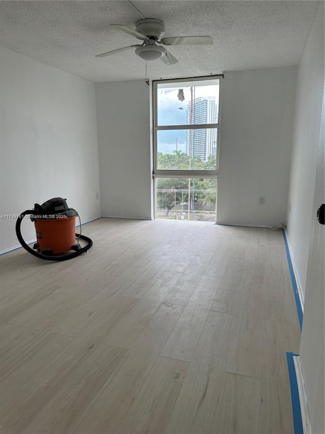 spare room featuring ceiling fan, light wood-type flooring, a textured ceiling, and a wall of windows