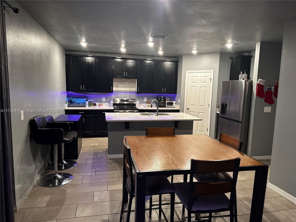 kitchen with sink, backsplash, stainless steel appliances, extractor fan, and an island with sink