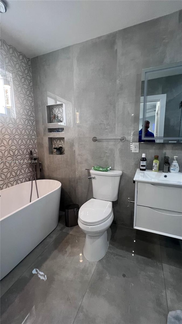 bathroom with toilet, concrete floors, tile walls, vanity, and a tub