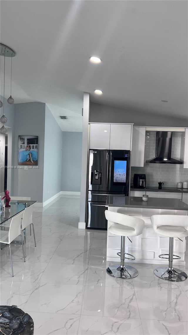 kitchen featuring a breakfast bar, pendant lighting, white cabinets, black fridge with ice dispenser, and wall chimney range hood