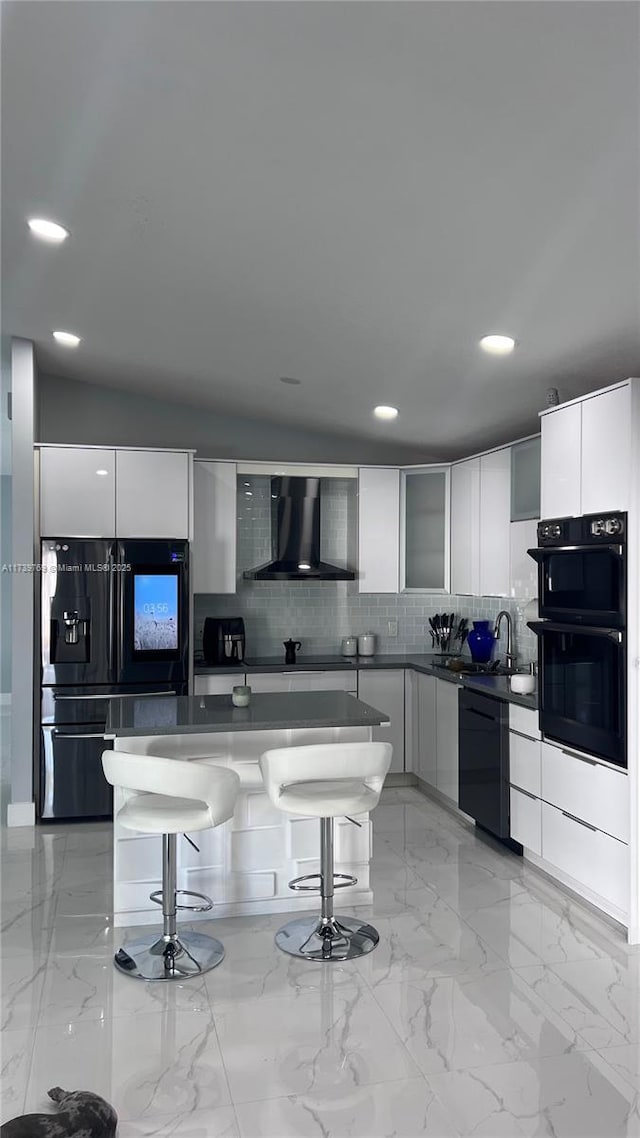 kitchen with white cabinetry, black appliances, wall chimney exhaust hood, and a kitchen bar