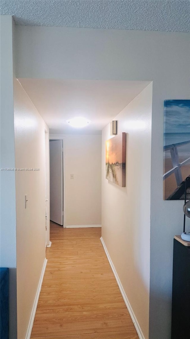 hall with a textured ceiling and light wood-type flooring