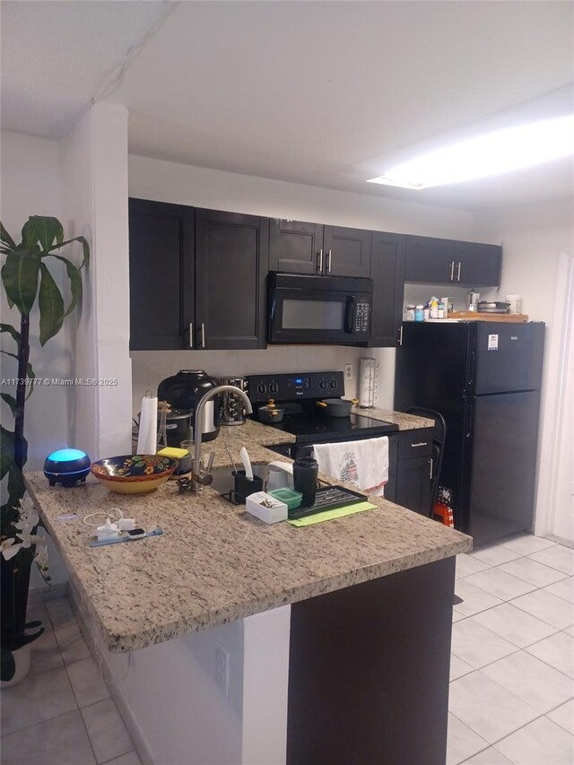 kitchen with light tile patterned floors, black appliances, kitchen peninsula, and light stone countertops