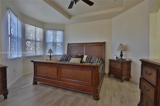 bedroom with light hardwood / wood-style floors, a raised ceiling, and ceiling fan