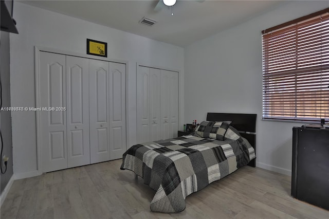 bedroom featuring ceiling fan, light wood-type flooring, and two closets