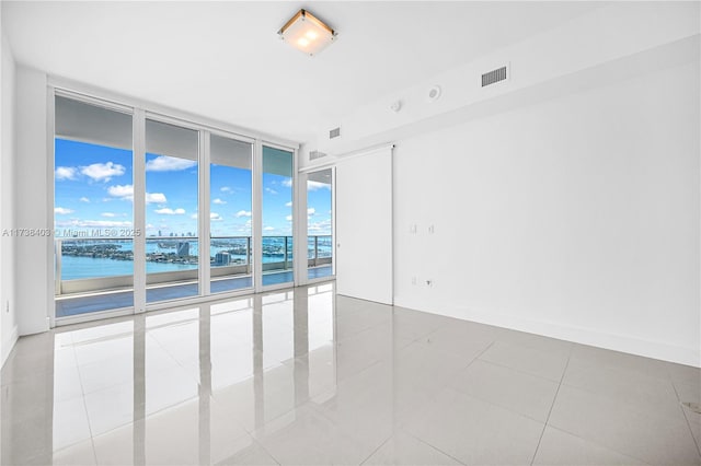 spare room featuring light tile patterned floors, a wall of windows, and a water view