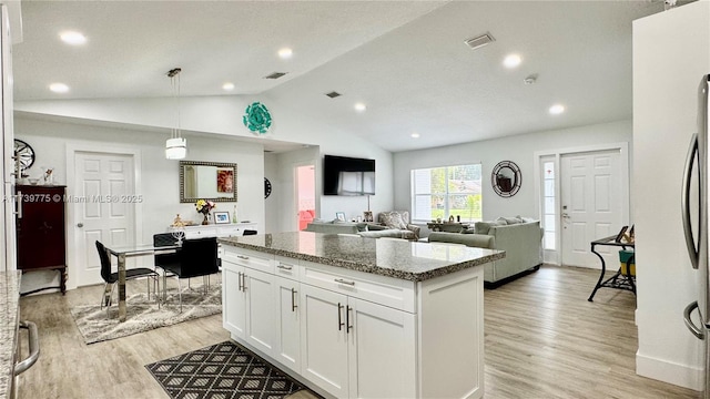 kitchen with a center island, lofted ceiling, stone counters, light wood-style flooring, and white cabinetry