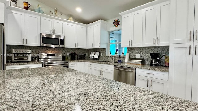 kitchen with light stone counters, stainless steel appliances, decorative backsplash, vaulted ceiling, and white cabinets