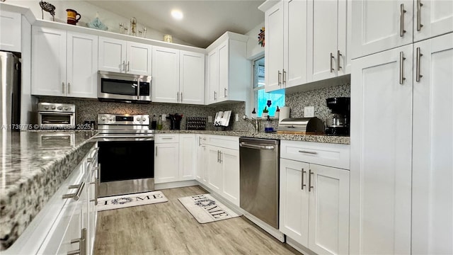 kitchen with tasteful backsplash, stainless steel appliances, light wood-style floors, white cabinets, and vaulted ceiling