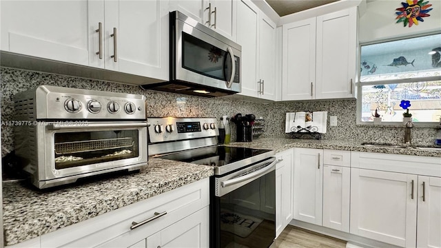 kitchen with a sink, backsplash, white cabinetry, stainless steel appliances, and light stone countertops