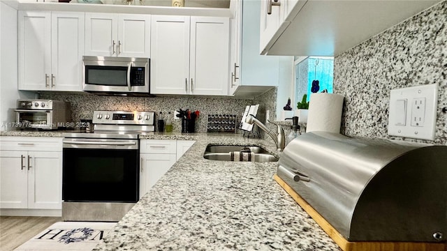 kitchen featuring sink, white cabinetry, appliances with stainless steel finishes, light stone countertops, and backsplash