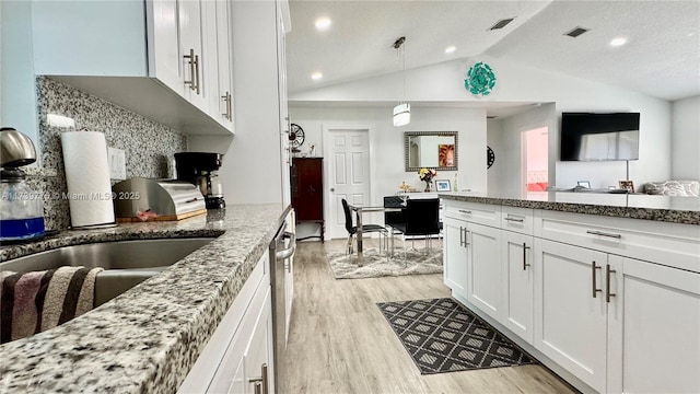 kitchen with lofted ceiling, white cabinetry, light stone counters, hanging light fixtures, and light wood-type flooring