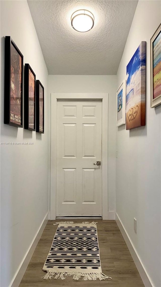 doorway to outside with a textured ceiling, baseboards, and wood finished floors