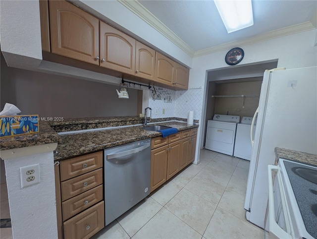 kitchen featuring sink, dark stone counters, ornamental molding, washing machine and dryer, and white appliances